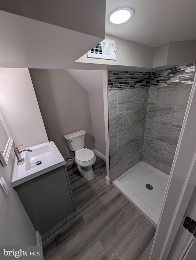 bathroom with toilet, a tile shower, wood-type flooring, and vanity