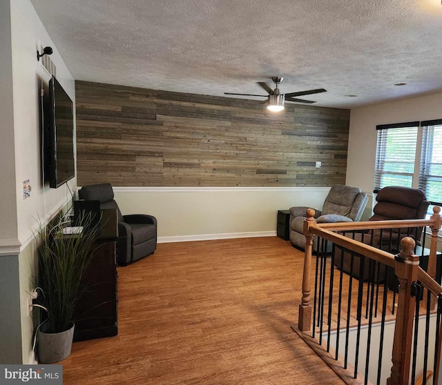 living room featuring ceiling fan, wood-type flooring, a textured ceiling, and wood walls