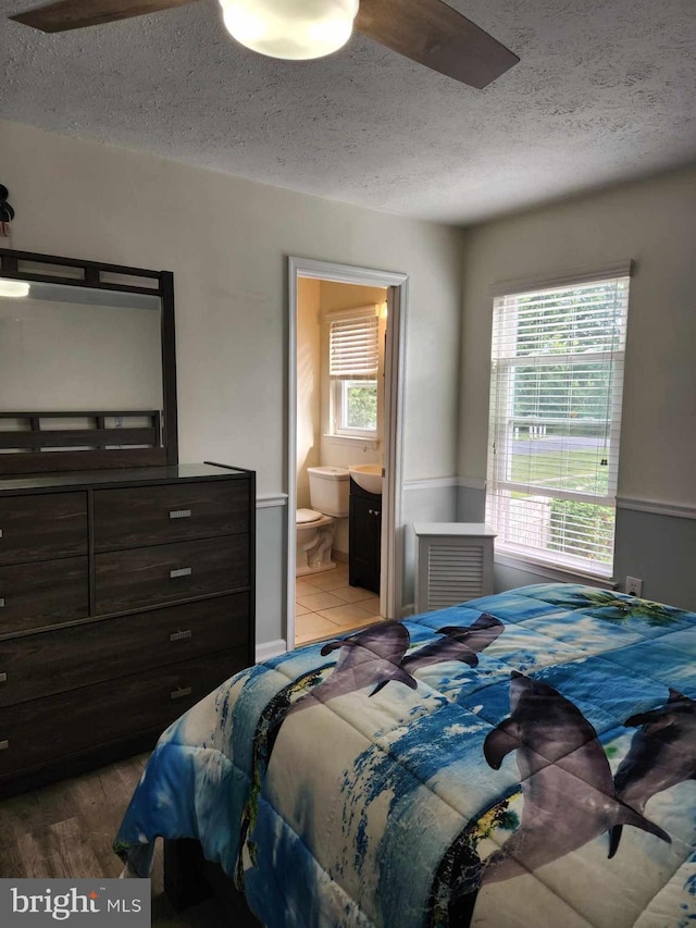 bedroom featuring multiple windows, connected bathroom, hardwood / wood-style flooring, and a textured ceiling