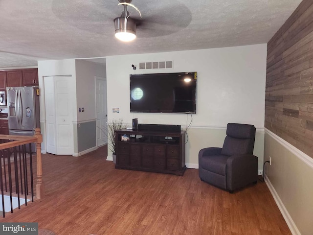 living room with wood-type flooring, a textured ceiling, and wood walls