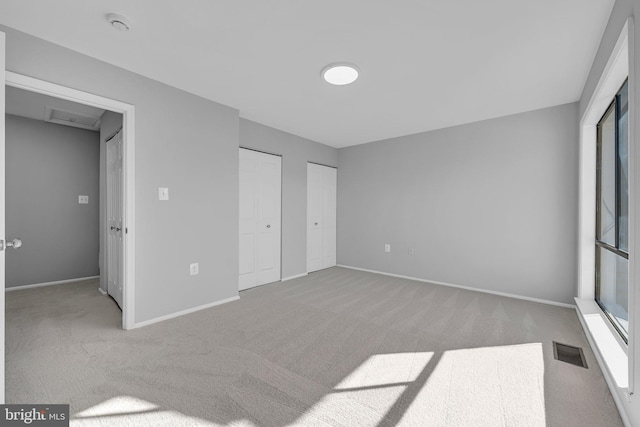 unfurnished bedroom featuring light carpet and multiple closets