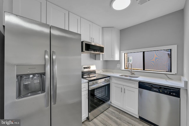 kitchen with appliances with stainless steel finishes, sink, white cabinetry, light stone counters, and light hardwood / wood-style floors