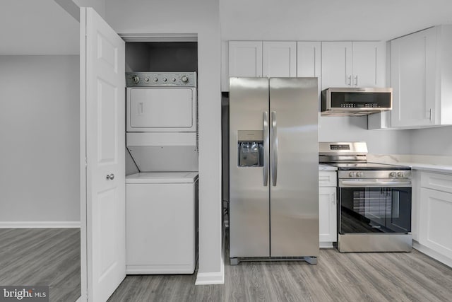 kitchen with white cabinets, light wood-type flooring, stacked washer and dryer, and stainless steel appliances