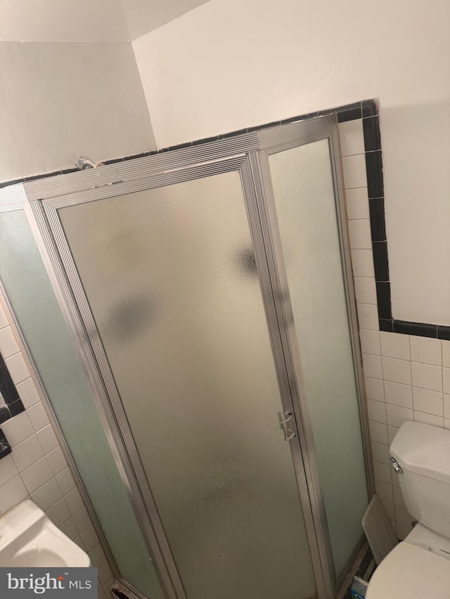 bathroom featuring toilet, a shower stall, and tile walls