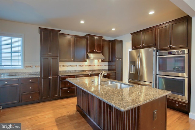 kitchen with sink, a center island with sink, light hardwood / wood-style floors, decorative backsplash, and stainless steel appliances