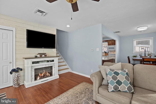 living room with wood walls, hardwood / wood-style flooring, ceiling fan, and a premium fireplace