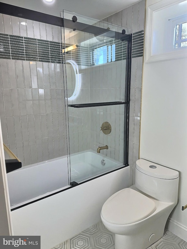 bathroom featuring toilet, bath / shower combo with glass door, and tile patterned flooring