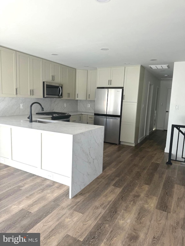 kitchen with backsplash, kitchen peninsula, dark hardwood / wood-style floors, and stainless steel appliances