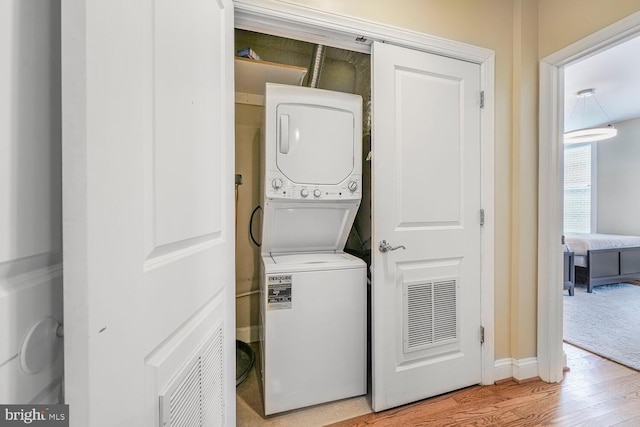 washroom featuring visible vents, baseboards, laundry area, light wood-style flooring, and stacked washing maching and dryer