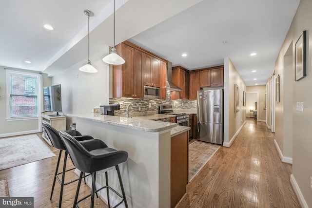 kitchen featuring backsplash, light stone countertops, appliances with stainless steel finishes, a peninsula, and light wood-style floors