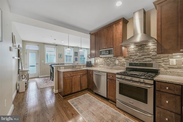 kitchen featuring a sink, tasteful backsplash, appliances with stainless steel finishes, a peninsula, and wall chimney range hood