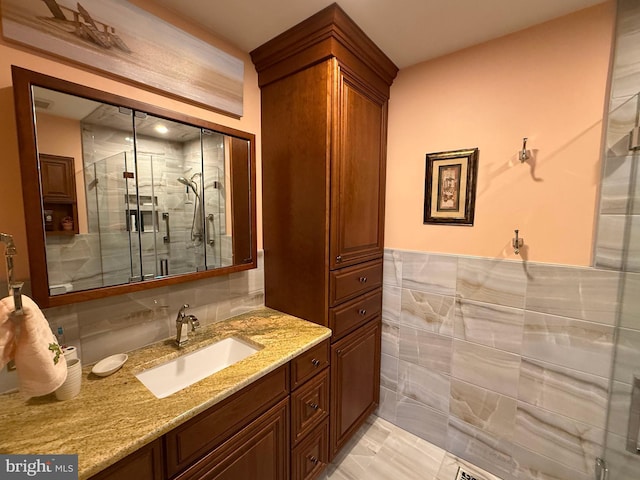 bathroom featuring a shower with door, vanity, and tile walls