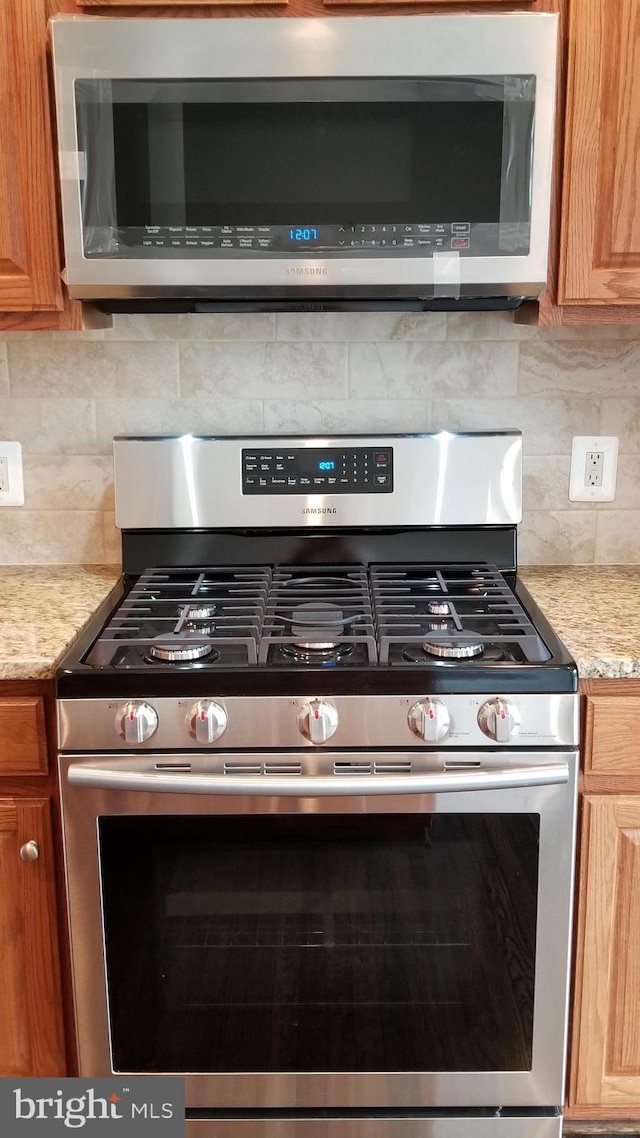 interior space with backsplash, appliances with stainless steel finishes, and light stone counters