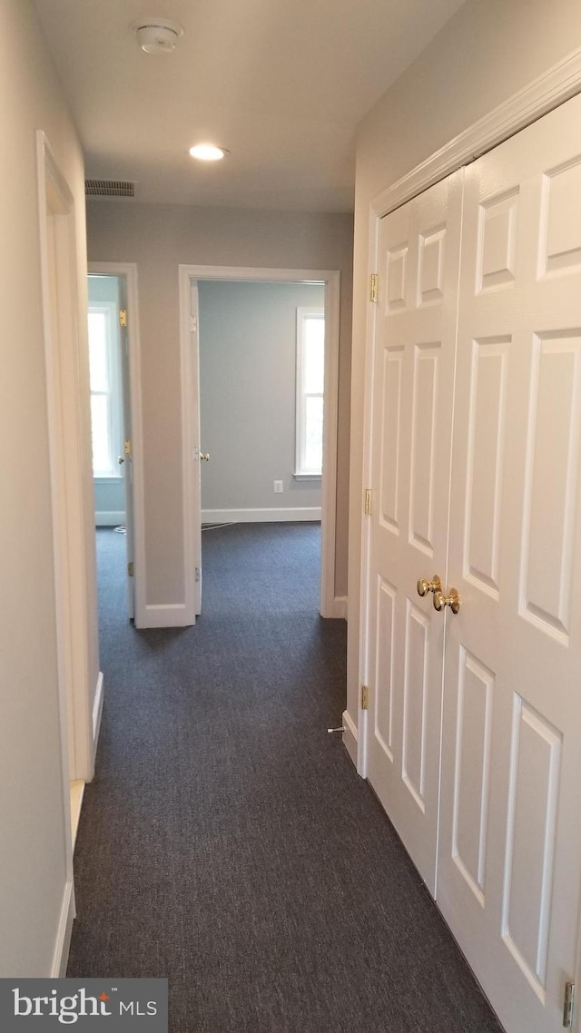 hall featuring dark colored carpet and plenty of natural light