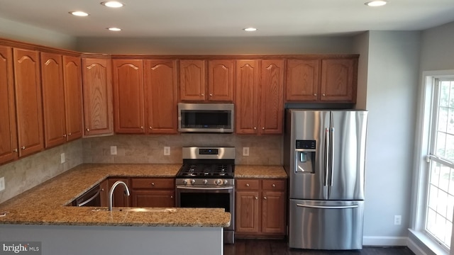 kitchen featuring stainless steel appliances, sink, tasteful backsplash, and light stone countertops