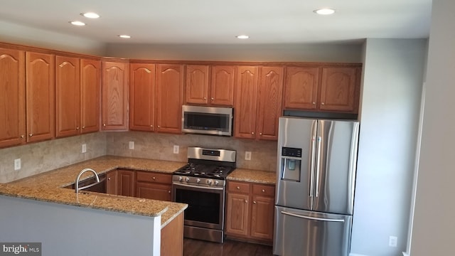 kitchen with light stone countertops, stainless steel appliances, sink, backsplash, and kitchen peninsula