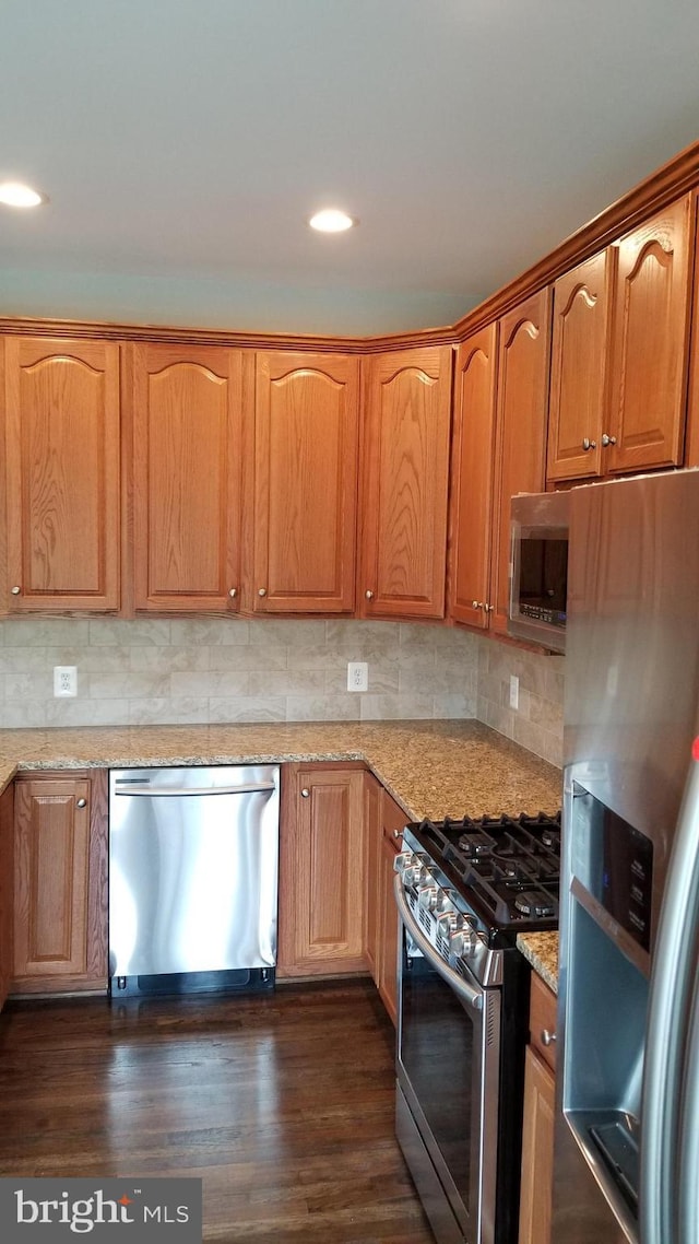 kitchen with light stone counters, decorative backsplash, appliances with stainless steel finishes, and dark hardwood / wood-style flooring