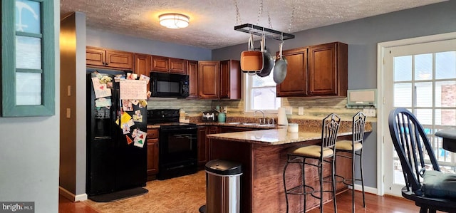 kitchen with kitchen peninsula, tasteful backsplash, decorative light fixtures, black appliances, and sink