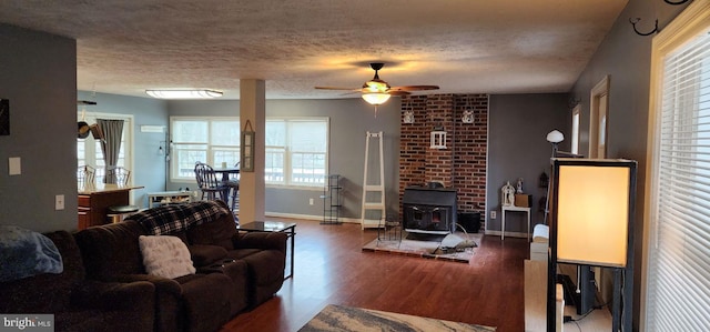 living room with ceiling fan, dark hardwood / wood-style flooring, a wood stove, and a textured ceiling