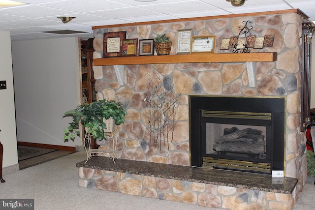 interior details with carpet, a drop ceiling, and a stone fireplace