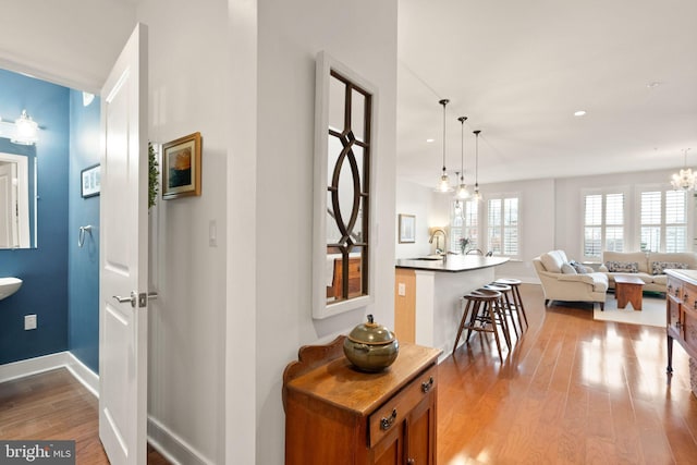 hallway with light wood-type flooring, a notable chandelier, and sink