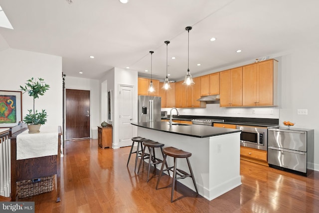 kitchen with an island with sink, stainless steel appliances, tasteful backsplash, decorative light fixtures, and sink