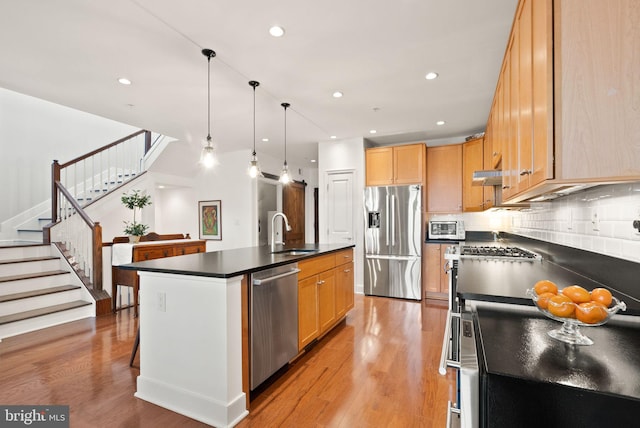 kitchen featuring pendant lighting, appliances with stainless steel finishes, light hardwood / wood-style floors, sink, and a kitchen island with sink