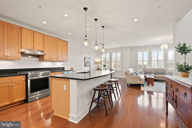 kitchen featuring a notable chandelier, stainless steel electric range, a breakfast bar, wood-type flooring, and an island with sink