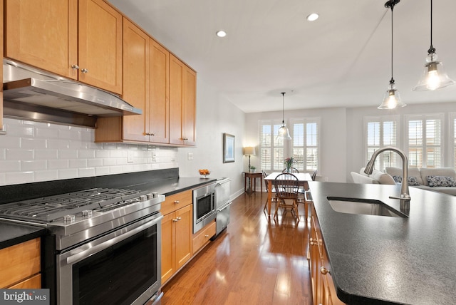 kitchen with decorative light fixtures, stainless steel appliances, sink, backsplash, and light hardwood / wood-style flooring