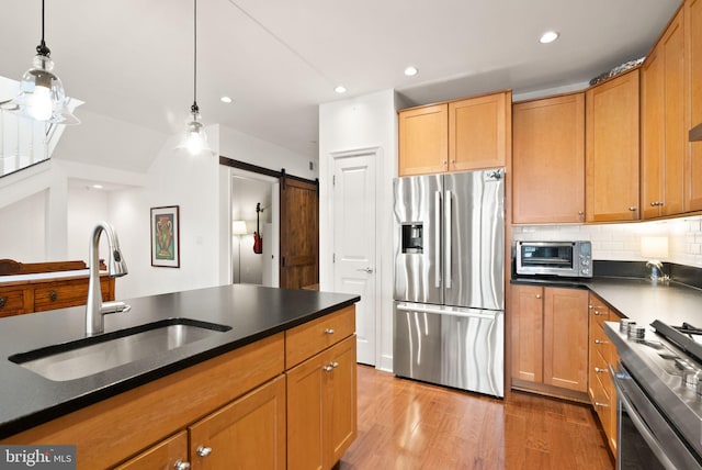 kitchen with pendant lighting, stainless steel appliances, tasteful backsplash, sink, and a barn door