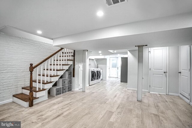 basement with brick wall, separate washer and dryer, and light wood-type flooring