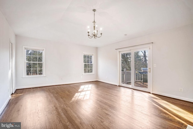 empty room with a notable chandelier, dark hardwood / wood-style floors, and a healthy amount of sunlight