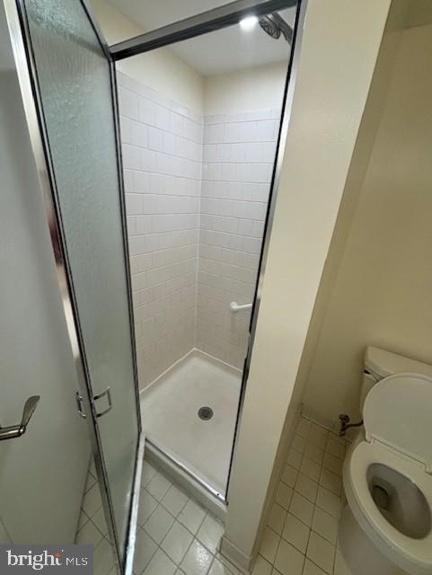 bathroom with tile patterned flooring, a shower with shower door, and toilet