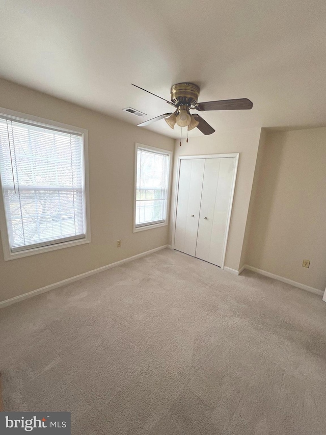 unfurnished bedroom with ceiling fan, multiple windows, a closet, and light carpet