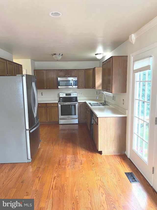 kitchen with light hardwood / wood-style floors, sink, crown molding, and stainless steel appliances