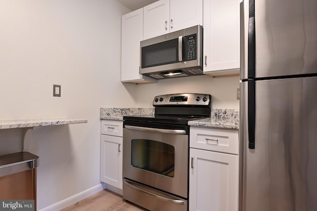 kitchen with baseboards, light wood-type flooring, light stone counters, white cabinets, and stainless steel appliances