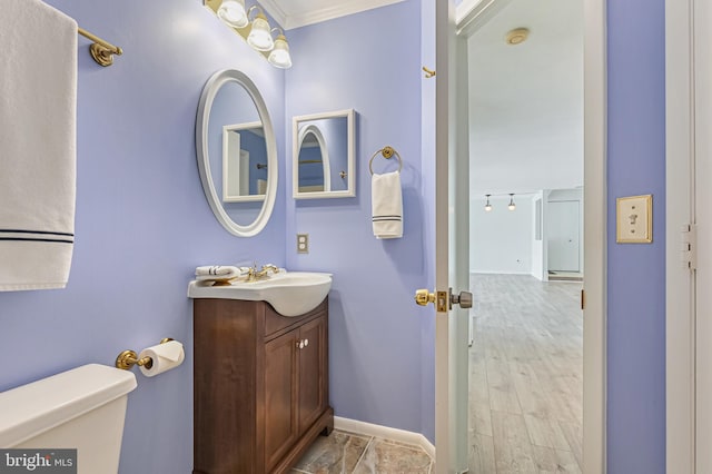 bathroom with vanity, wood finished floors, baseboards, crown molding, and toilet