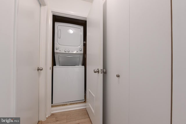 clothes washing area featuring laundry area, stacked washer and clothes dryer, light wood-type flooring, and visible vents