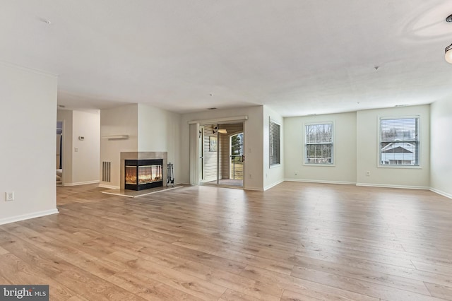 unfurnished living room with a multi sided fireplace, visible vents, light wood-type flooring, and baseboards