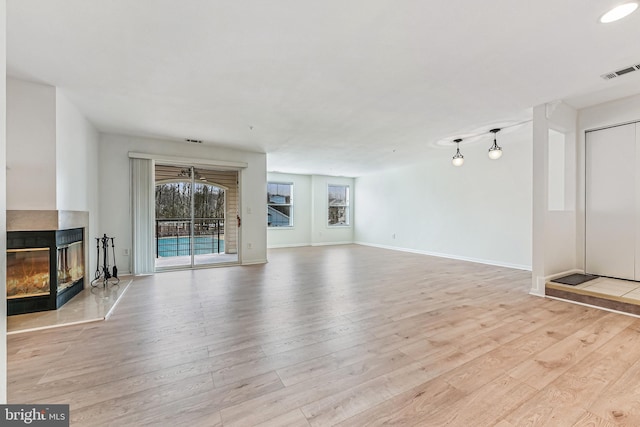 unfurnished living room with visible vents, a multi sided fireplace, baseboards, and wood finished floors