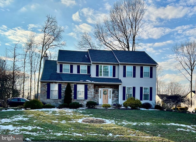 view of front facade with a front yard, stone siding, and a chimney