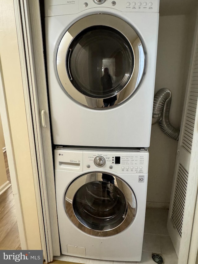 clothes washing area with stacked washer and clothes dryer and light tile patterned floors