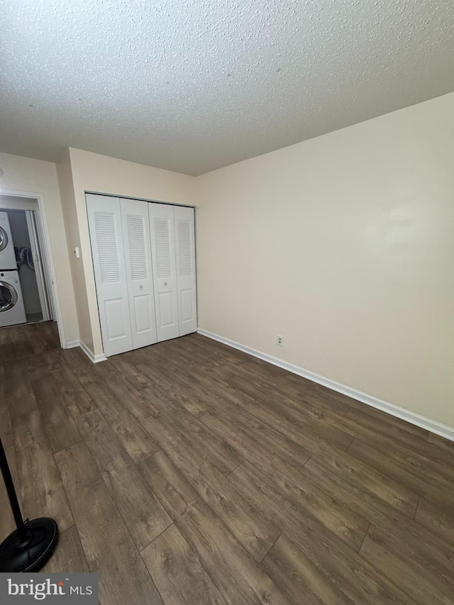 unfurnished bedroom with stacked washer / dryer, a textured ceiling, a closet, and dark hardwood / wood-style flooring