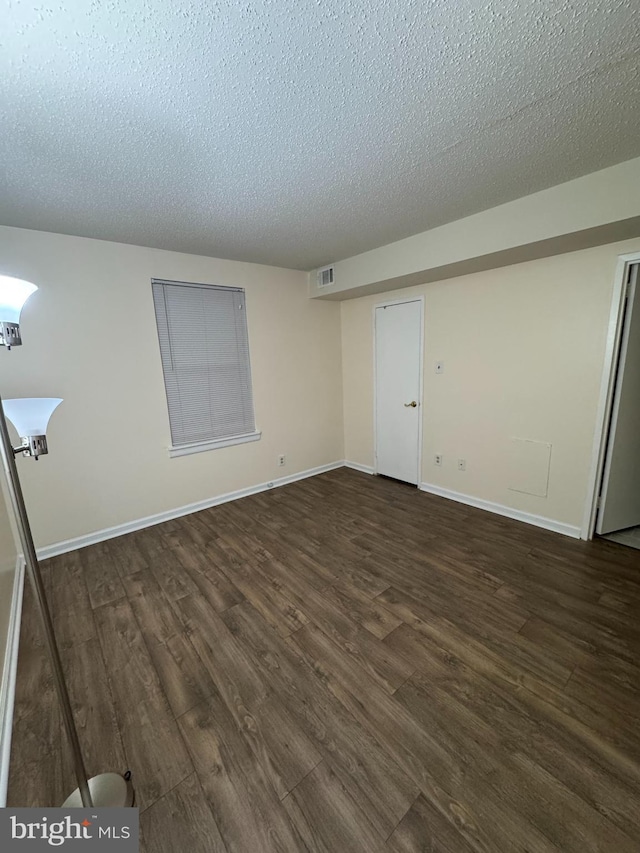 unfurnished room featuring a textured ceiling and dark hardwood / wood-style flooring