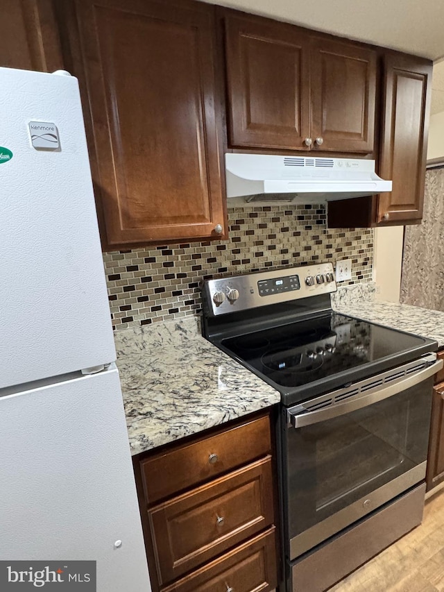 kitchen with light stone countertops, white fridge, stainless steel electric range, decorative backsplash, and light hardwood / wood-style flooring