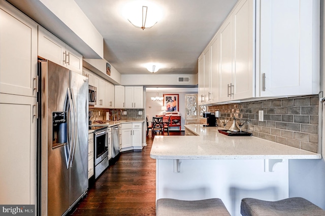 kitchen with appliances with stainless steel finishes, white cabinetry, decorative backsplash, a kitchen breakfast bar, and kitchen peninsula