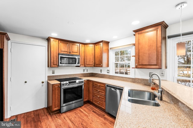 kitchen with light stone countertops, hardwood / wood-style floors, stainless steel appliances, sink, and hanging light fixtures