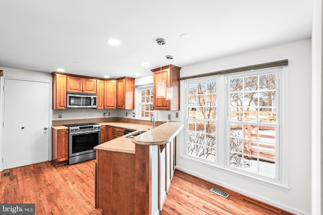 kitchen with light hardwood / wood-style floors, kitchen peninsula, sink, hanging light fixtures, and stainless steel appliances