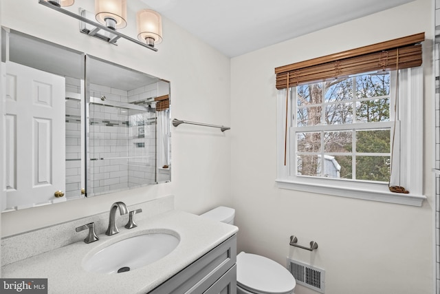 bathroom featuring toilet, vanity, and a shower with door