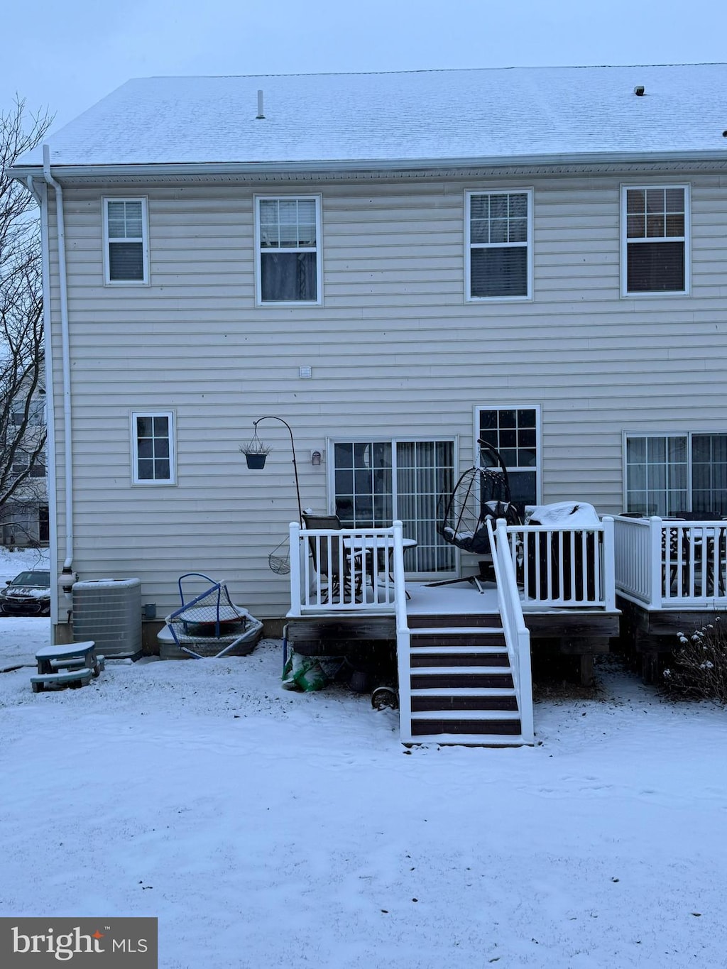 snow covered rear of property with a wooden deck, cooling unit, and a fire pit